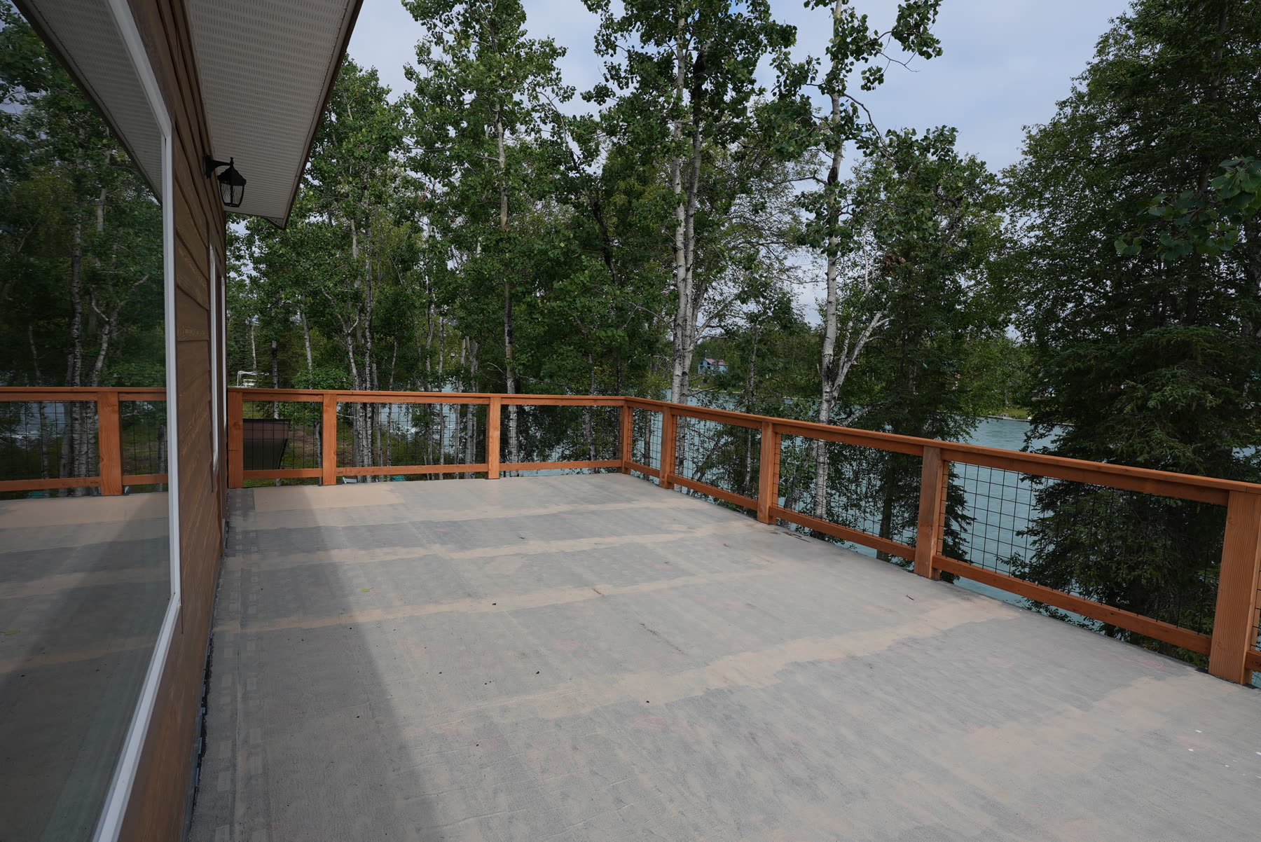 Wide wooden deck with railing overlooking trees and the river